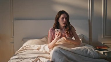 Uyuyakalan kız, acele et, yatak odası sabah. Geç saatte konuşan cep telefonlu kadın altın güneş ışığında yataktan fırladı. Şok olmuş genç model paniğe kapıldı. Endişeli bayan çalar saat.