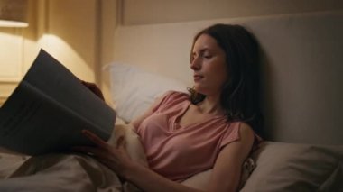 Yatakta kitap okuyan gülümseyen kız. Yakın plan. Rahat bir kadın, rahat evinde rahat bir uyku çekerek romanının tadını çıkarıyor. Huzurlu sakin bayan öğrenci, sayfayı çevirerek geç saatlere kadar ders çalışıyor. Uyum hobisi.