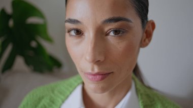 Sadece evde poz veren pozitif kadın portresi. Kameraya bakan esmer kız yeşil bitkilerin dairesinde kendini rahat hissediyor. Sakin genç bayan, kanepede oturup dinleniyor.