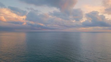 Nefes kesici okyanus gündoğumu panoramik dron görüntüsü. Gri bulutlar arasında parıldayan altın güneş ışığı dramatik bir yaz sabahında. Sakin deniz ufku yavaş çekim. Sakin derin mavi deniz manzarası