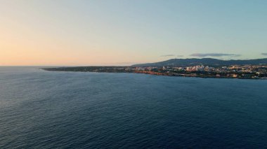 Sakin deniz akşamı deniz kenarı kasabası. Havadan panoramik manzara şafak vakti pastel gökyüzü güzel günbatımı sahili üzerinde. Resimli bir okyanus manzarası, tatil köyü ağır çekimde. Deniz kıyıları sakin suyla yıkanır.