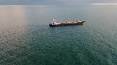 Hava manzaralı kargo gemisi kasvetli ufukta okyanusa yelken açıyor. Sakin dalgalı deniz yüzeyinde yüzen büyük bir konteyner tankeri. Panoramik gemi yaz manzarasında derin suları hareket ettiriyor. Denizcilik lojistiği