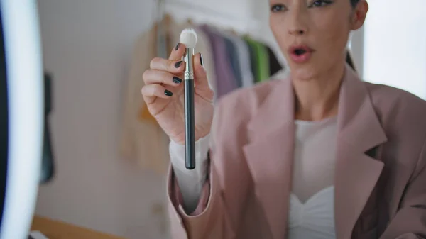 Talking woman recording videoblog at room close up. Smiling lady influencer presenting makeup brush reviewing product to mobile phone at home. Trendy blogger holding visage equipment giving advices