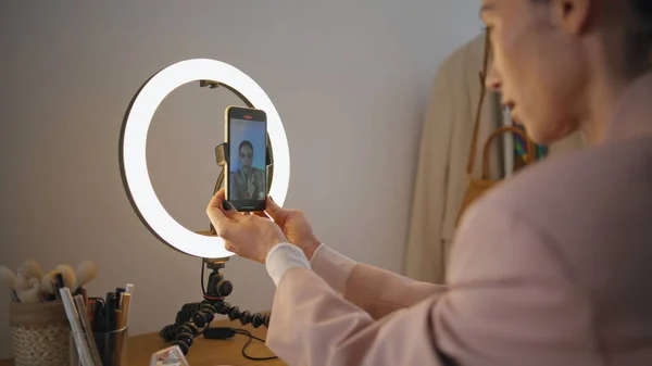 Creative blogger recording mobile phone video at home closeup. Influencer lady adjusting smartphone on round light stand at workplace zoom on. Calm woman pushing button started live stream translation