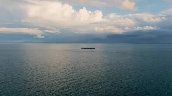 Aerial view bulk carrier ship sailing at cloudy day. Big cargo vessel floating dark deep ocean at gloomy summer. Contrast sunlight breaking grey clouds reflecting in sea surface. Beauty marine nature