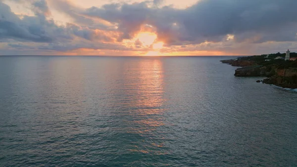 Dramatik bulutlu deniz panorama drone görüntüsü. Altın güneş ışığı kıran gri gök gürültüsü bulutları sakin deniz suyu yüzeyine yansıyor. Ağır çekimde dalgalanan karanlık okyanus manzarası. İnanılmaz yaz sabahı deniz manzarası