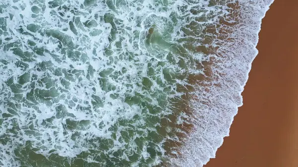 White ocean foam waving at sandy beach close up. Aerial deep dark water rolling seashore foaming. Top view beautiful seaside landscape with stormy sea splashing waves. Dramatic marine scenery concept