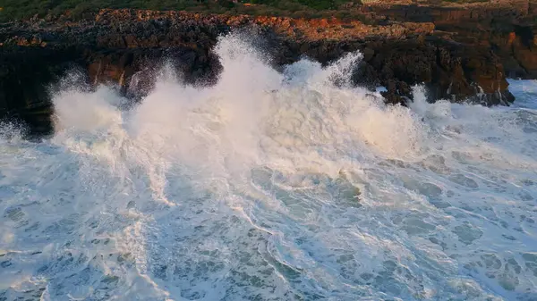 Drone view rough ocean waves crashing on coastal cliffs slow motion. Majestic sea surf lapping on rocky beach closeup. Fabulous tide breaking on seashore making white high foam. Coastal nature scenery