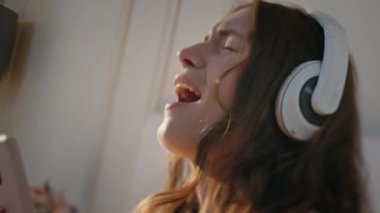Evde kulaklık takan mutlu bir kız. Enerjik, güzel bayan dans, gün ışığında en sevdiği ritim şarkısına geçiyor. Neşeli genç bir kadın hafta sonu müzik dinlemekten hoşlanıyor. Yaşam tarzı eğlence konsepti.
