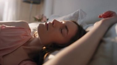Sabah kızı, güneş ışığında gözlerini aç. Yakın plan. Huzurlu gülümseyen kadın rahat bir yatakta kameraya bakarak uyanıyor. Huzurlu, güzel bir model hafta sonunun keyfini çıkarıyor. Tembel tatil yaşam tarzı konsepti.