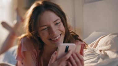 Neşeli kız evde akıllı telefonu yakın planda tutuyor. Gülücükler saçan romantik bir kadın sabah güneşinde sevişmeyi düşünür. Çekici, mutlu bir kadın cep telefonuna sarılıyor, içeride hayal kuruyor..