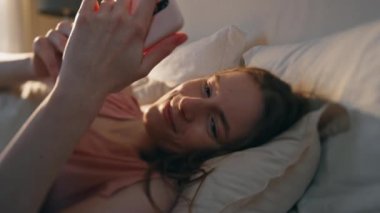 Mutlu kız yatakta akıllı telefon ekranına benziyor. Uykulu kadın mesaj sarılma hücresini okuyor. Güzel sakin kadın sabah cep telefonuyla kontrol et. Uyanık model genç rüya görüyor İyi haberlerin tadını çıkar.