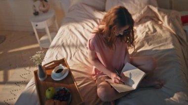 Evde günlük yazan düşünceli bir kadın. Rahat genç kız, yaratıcı fikirleri not defterinde paylaşıyor. Keyifli odaklı kadın planlama samimi yatak odasında notlar alıyor. Sabah ilham konsepti.