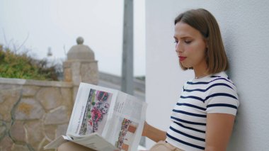 Dışarıda gazete okuyan odaklanmış bir kız. Güzel bir turist sabah yerel bir dergiyi kontrol ediyor. Kaygısız kadın terasta dinleniyor ve tatilin tadını çıkarıyor. Huzurlu hafta sonu konsepti.