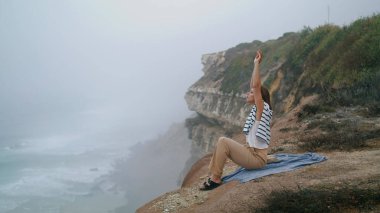 Yaz tatilinde deniz kayalıklarını geren bir kadın. Sakin turistler deniz kıyısındaki piknikte hayatın tadını çıkarıyorlar. Huzurlu güzel kız kayalık tepede tek başına rahatlıyor. Huzurlu yaşam tarzı konsepti