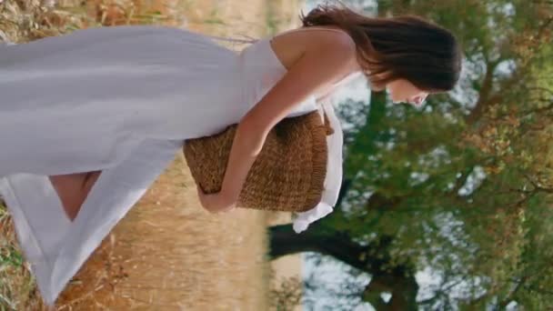 洗濯物のバスケットを持っている若い女性は垂直に乾燥した草の庭を歩きます 穏やかな官能的な少女は小麦のスパイレットフィールドでゆっくりと踏み出しているカメラを見ます 農村の主婦はウィッカーパニエ交差ライメドウを運ぶ — ストック動画