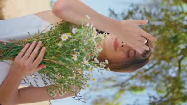 Portrait belle femme embrassant des fleurs douces dans la nature rurale. Grosse dame souriante verticale avec bouquet de camomilles printanières fraîches au soleil. Fille heureuse profitant bourgeons floraux redresser les cheveux venteux