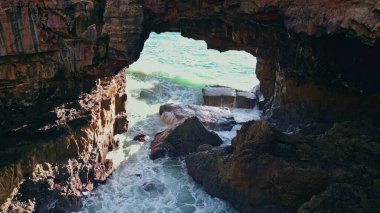 Dev bir okyanus dalgası, çok yavaş bir şekilde köpüren karanlık sahil kayalıklarını kırıyor. Fırtınalı köpüklü su volkanik kayalara çarpıyor. Resimli manzara güçlü deniz kabaran yaz günü.