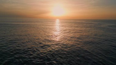 Sabah deniz dalgaları yavaş çekimde sıçrıyor. Güneşin doğuşuyla dalgalanan deniz dalgaları, hava görüntüsünü yakınlaştırır. Turuncu güneş ışınlarının altında yüzen manzaralı derin su. Karanlık okyanus yüzeyi pastel ışığı yansıtıyor. 