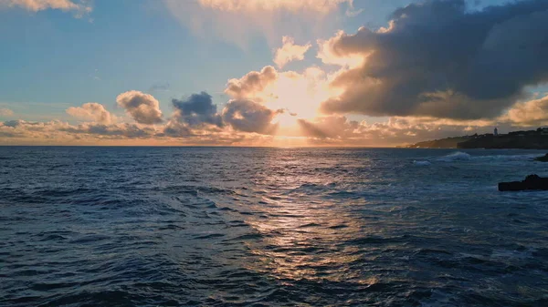Amazing bright marine sunset over deep dark ocean surface reflecting golden evening light. Aerial view sun rays breaking through clouds shining on sea water slow motion. Beautiful summer vacation.