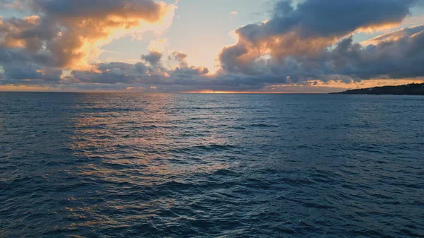 Cloudy evening sky over ocean water rippling waving in slow motion. Drone view powerful endless dark sea at summer sunset. Gray clouds hanging over marine horizon hiding sunlight. Tranquility concept.