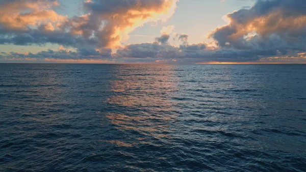 Drone view tranquil ocean waves under cloudy sky early morning. Deep dark sea rippling at summer sunrise slow motion. Wonderful marine twilight at endless water. Golden sunlight shining far at horizon