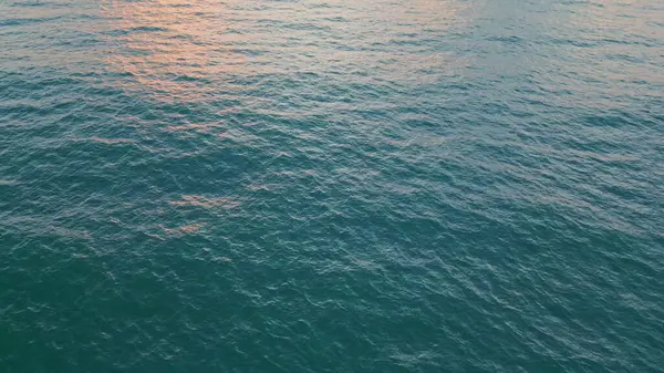 Dark ocean water rippling under golden evening sky in slow motion. Aerial view picturesque marine sunset reflecting in calm sea surface. Heavy clouds hanging over endless ocean horizon. Travel concept