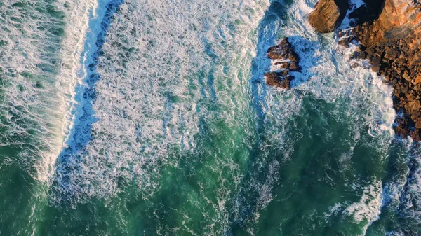 Top view waves barrelling to volcanic cliffs in super slow motion. Drone shot beautiful powerful sea water splashing rocky coastline crashing stones. Sunny marine scenery dangerous rugged shoreline