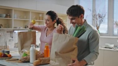 Mutfak masasına alışveriş yapan bir çift marketten yakın mesafeden geldi. Gülümseyen aile, ev mutfağında eko-kağıt paketleri açıyor. Mutlu eşler yemek pişirmek için tezgahta yemek sıralıyorlar..