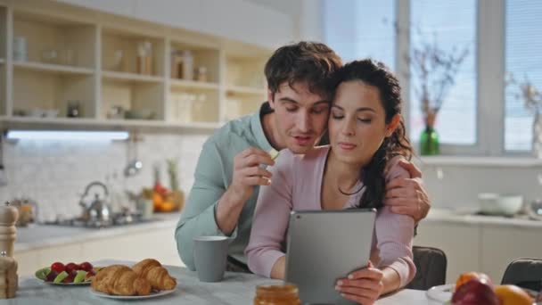 若いカップルは 近代的なタブレットスタンディングホームキッチンクローズアップを使用してビデオミーティングで挨拶 リラックスした素敵な配偶者は 屋内での朝食で友人と通話するオンライン通話を持っています ファミリーウェブチャット — ストック動画