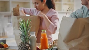 Teslimatı yapan çiftler mutfaktaki konforlu ürünleri birlikte yerleştiriyorlar. Tezgahtaki kağıt paketten organik yemek alan gülen eşler. Çevrimiçi süpermarket alışveriş hizmetleri kavramı.