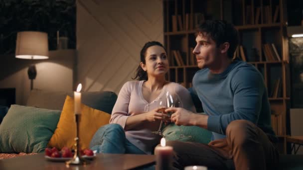 爱喝红酒的夫妻坐在沙发上 点着蜡烛 快乐的两个恋爱中的人在家里享受浪漫的夜晚 迷人温柔的男朋友和漂亮的女朋友高脚杯聊天 — 图库视频影像