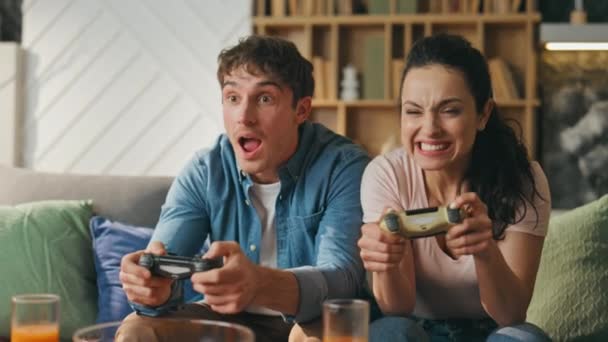 既婚のゲーマーは ホームソファーの近くに座っているビデオゲームを楽しんでいます かわいい妻は コンソールを投げなかったことに失望した 笑顔の夫がビデオゲームの勝利を喜びました ファミリーエンターテイメントコンセプト — ストック動画