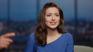 Gülümseyen kadın sunucu sohbet programı izleyicileriyle etkileşime giriyor modern TV stüdyosunda misafirlerle yakın çekim yapıyor. Programda adı bilinmeyen ünlüleri dinleyen genç bir spiker var. Eğlence kanalı.
