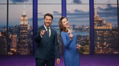 Televizyon kanalında gülümseyen iki haber spikeri. Gülümseyen çift sunucuları haber bültenini sunuyor ayakta sahne TV stüdyosu. Havada işbirliği yapan karizmatik mutlu sunucular konuşuyor..
