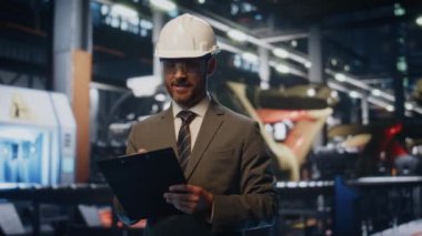 Kontrol listesi olan mutlu fabrika müfettişi üretim ekipmanlarını inceliyor. Modern makinelerin gülümsemesine bakan kasklı, tatmin olmuş bir denetçi. Sakallı patron, fabrikayı kontrol ediyor..