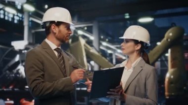 Fabrika patronu koruyucu kasklı kadın mühendis ile el sıkışıyor. İki iş adamı üretim alanında sözleşme imzalıyor. Kendinden emin ortaklar gülümsüyor..