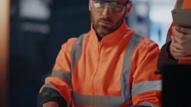 Fabrika uzmanı bilgisayardan tabletli kadın mühendise teknik verileri gösteriyor. Endüstriyel fabrika aletleri üzerinde çalışan iki üniformalı profesyonel teknisyen. Üretim takım çalışması kavramı