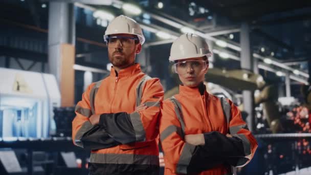 重工業の製造に従事する2人の工場労働者が制服を着た ヘルメットを身に着けている現代的な機械類の前に立っている自信のあるプロのカップル職人 植物スペシャリストの肖像画 — ストック動画