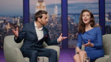 Talk show konuğu, televizyon stüdyosunda çekici bir sunucuyla oturan seyircilere başarılarını anlatıyor. Gülümseyen kadın sunucu erkeğin duygusal tepkisini dinliyor. Canlı yayında mutlu bir iş adamı.