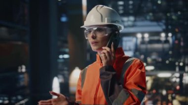 Gülümseyen teknisyen, fabrika deposundan cep telefonunu arıyor. Üniformalı mutlu kadın mühendis akıllı telefon konuşmasına gülüyor. Neşeli kadın prodüksiyon işçisi cep telefonundan konuşuyor.