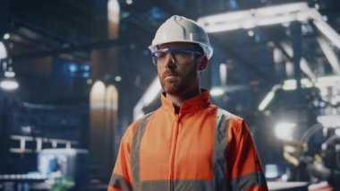 Büyük modern üretim atölyesinde kendine güvenen bir işadamı duruyor. Endüstriyel tesislerde poz veren profesyonel mühendis. Kasklı ciddi bir fabrika işçisinin portresi..