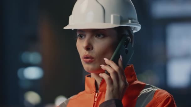 工厂的女商人穿着保护头盔制服在工厂里讲智能手机 认真的女工程师给合作伙伴打电话 讨论制造业项目的密切关注 女技术员发言 — 图库视频影像