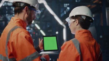 Metalurji fabrikasıyla ilgili teknik verileri tartışan iki mühendis tableti yakından inceliyor. Erkek teknisyen yeşil ekran bilgisayarda kadınlara üretim planını gösteriyor. Bir çift üniformalı yetenekli işçi.