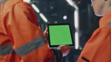 Ekip teknisyenleri endüstriyel tesislerdeki yeşil ekran tablet bilgilerini inceliyor. Tanımlanamayan mühendis kadın işçiye bilgisayar gösteriyor. İki üniformalı fabrika uzmanı..