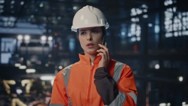 工厂员工在车间特写部讲手机 认真的女工程师 穿着制服 戴着安全帽 在生产车间打电话 利用智能手机讨论工作的年轻女技术员 — 图库视频影像