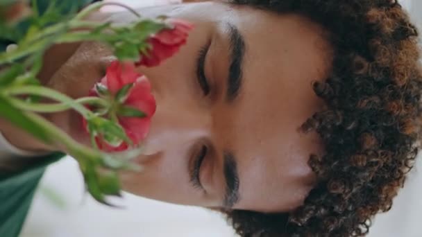 可爱的非洲男人喜欢在花店的垂直特写中喷洒玫瑰 卷发人在工厂商店里闻到春天的花束 俊俏的笑脸客户买花作曲 美丽快乐的爱情概念 — 图库视频影像