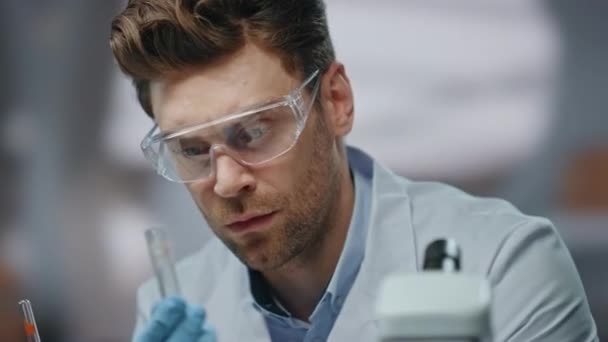 在生物化学实验室检查药物的闭塞科学家 年轻而严肃的研究人员拿着试管显微镜对样品进行观察 从事科学研究的安全眼镜实验室技术员 — 图库视频影像