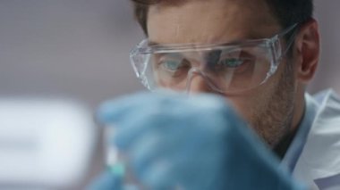 Klinik çalışanı test tüpündeki numune deneysel maddeyi analiz ediyor. Eldiven gözlüklü ciddi bir bilim adamı araştırma verilerini laboratuvar bilgisayarına giriyor. Koronavirüs aşısını inceleyen akıllı biyokimyacı..
