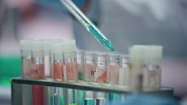 在先进的遗传学实验室进行填充物试管 无法辨认的科学家用吸盘滴疫苗样本到烧杯里 戴防护手套的实验室工作人员试用药物 — 图库视频影像